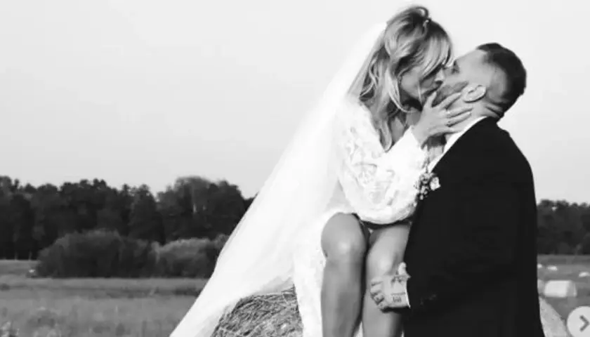 Patrycja Markowska i jej mąż w czułym uścisku na tle wiejskiego krajobrazu.