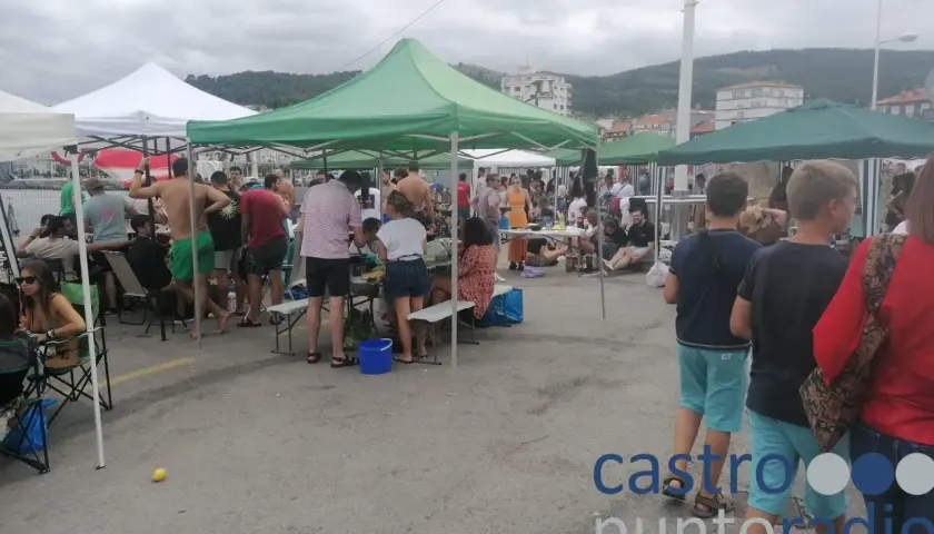 Gente reunida bajo carpas en un evento al aire libre en **Santa Ana, Castro Urdiales**. Un día nublado con ambiente festivo.