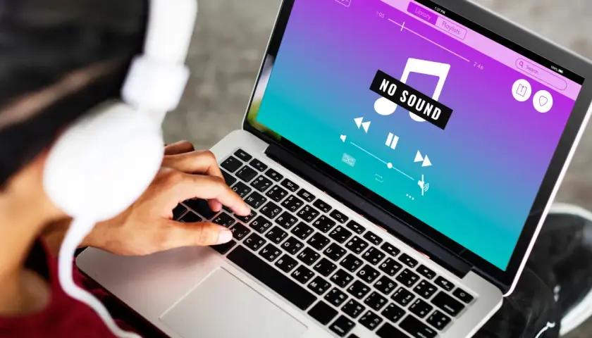 Osoba w słuchawkach próbuje rozwiązać problem **braku dźwięku w laptopie**, na ekranie widnieje komunikat "NO SOUND".