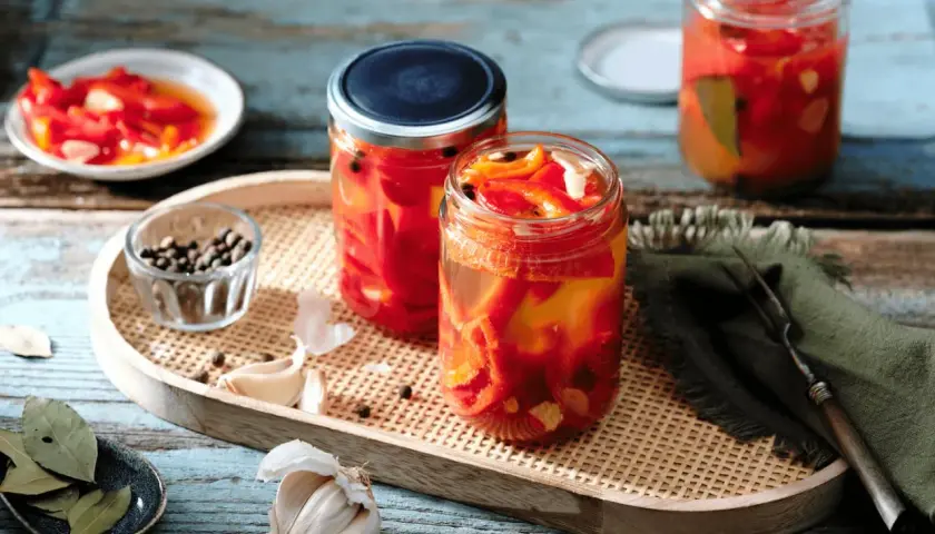Zwei Gläser mit eingelegten Paprikastreifen, Knoblauch, Pfefferkörnern und Lorbeerblättern. Der Prozess des Paprika fermentieren ist hier gut sichtbar.