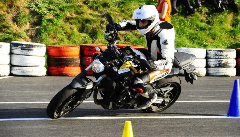 Motocyklista w białym kasku i kombinezonie doskonale opanował pozycję na motocyklu, pochylając się na zakręcie toru.