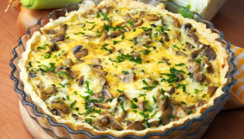 Pyszna tarta z pieczarkami i porem, posypana świeżą natką pietruszki, w szklanej formie.