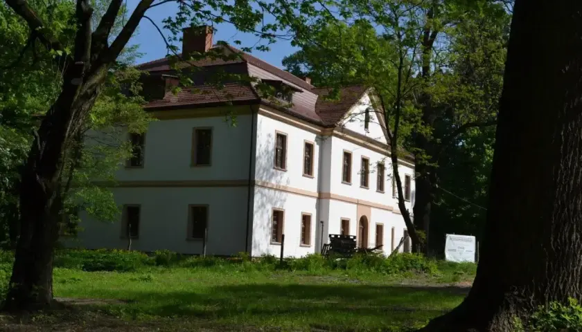 Dworek otoczony drzewami. Jak sprawdzić czy budynek jest zabytkiem? Sprawdź tablicę informacyjną obok.