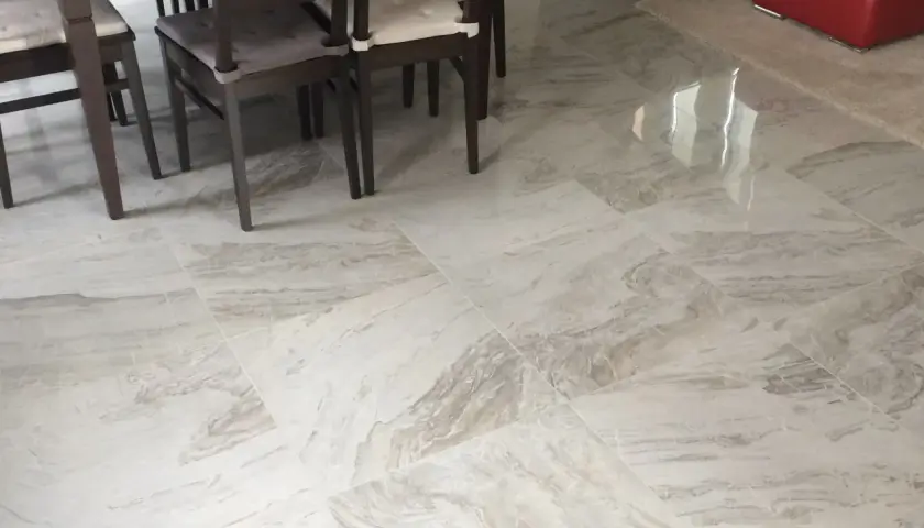 Pavimento in gres porcellanato effetto marmo, con venature grigie e bianche, sotto un tavolo con sedie scure.