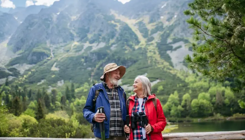 Szczęśliwa para seniorów na wczasach ze związku emerytów, podziwiająca górski krajobraz z jeziorem.