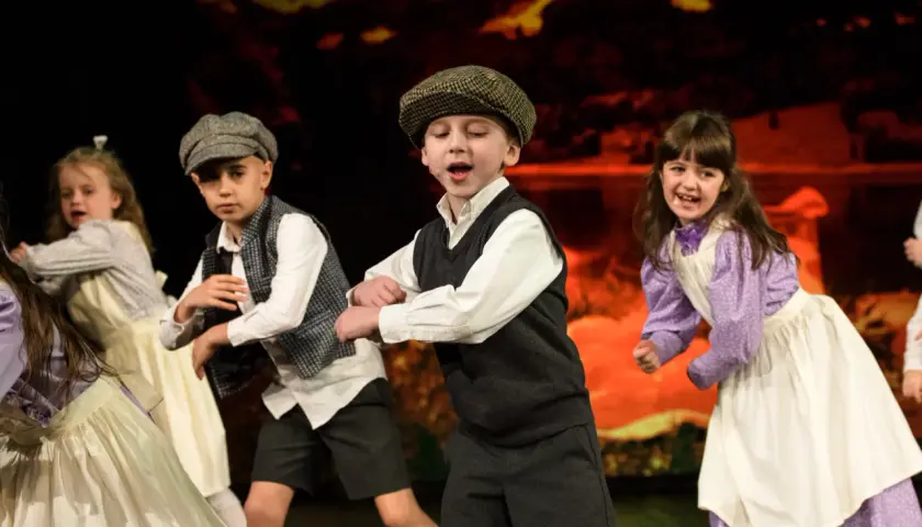 Dzieci w strojach teatralnych tańczą na scenie.