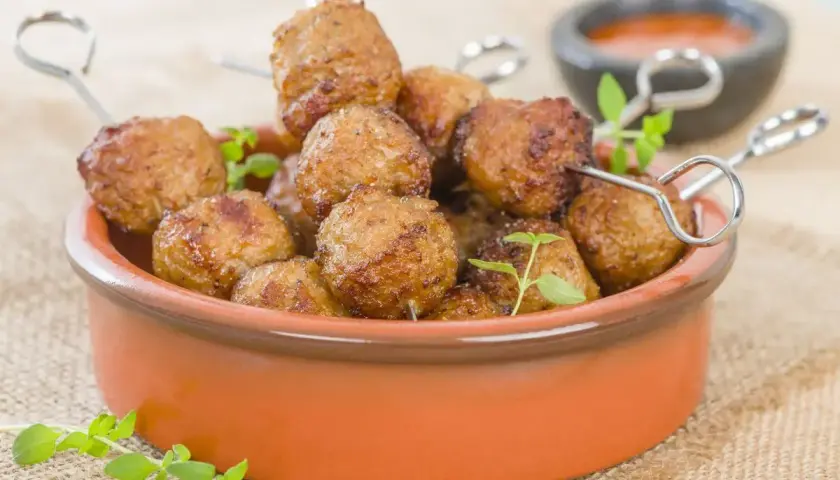 Polpette di tacchino dorate e succulente, cotte nella friggitrice ad aria, servite in una ciotola di terracotta con erbe aromatiche.
