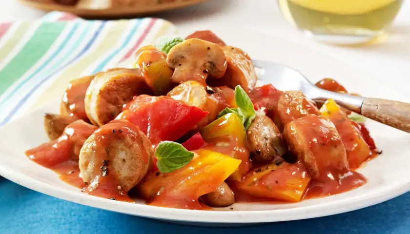 Herzhaftes Wurstgulasch mit Bratwurst, Tomaten und Pilzen, garniert mit frischen Kräutern. Ein deftiges Gericht für Genießer.