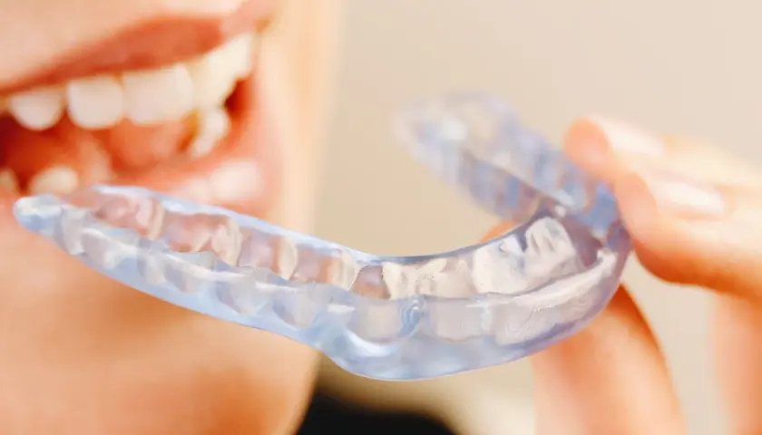 Persona sonriente sostiene una férula Invisalign transparente, lista para mejorar su sonrisa.