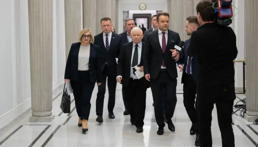 Politycy idą korytarzem, a kamerzysta nagrywa ich z tyłu. Widać, że idą w przeciwnych kierunkach, co jest ciekawe.