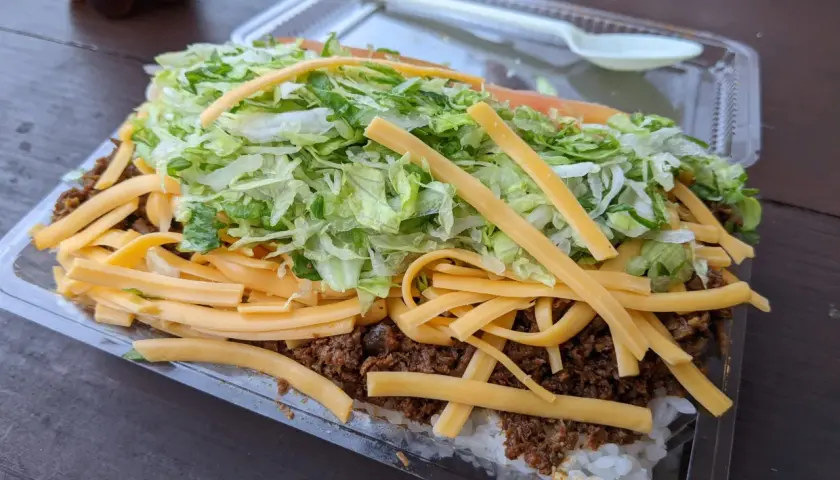 A hearty Okinawa taco rice dish, layered with white rice, seasoned ground meat, shredded lettuce, and melted cheese, ready to be enjoyed.