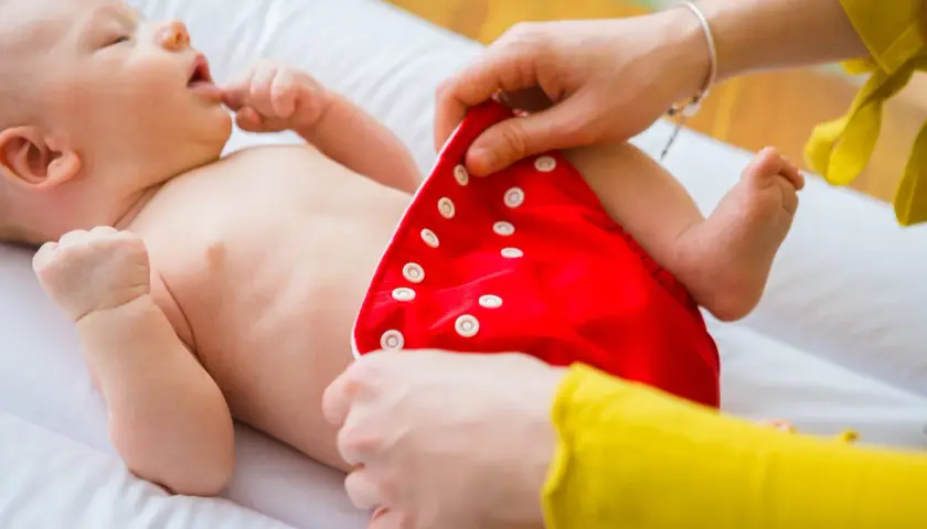 Mama zakłada dziecku czerwoną pieluchę tetrową. To pierwszy krok do tego, jak prać pieluchy tetrowe, by były czyste i ekologiczne.