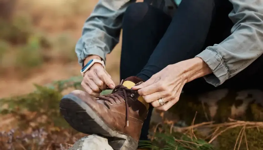 A person demonstrates how to lace boots, preparing for an outdoor adventure.