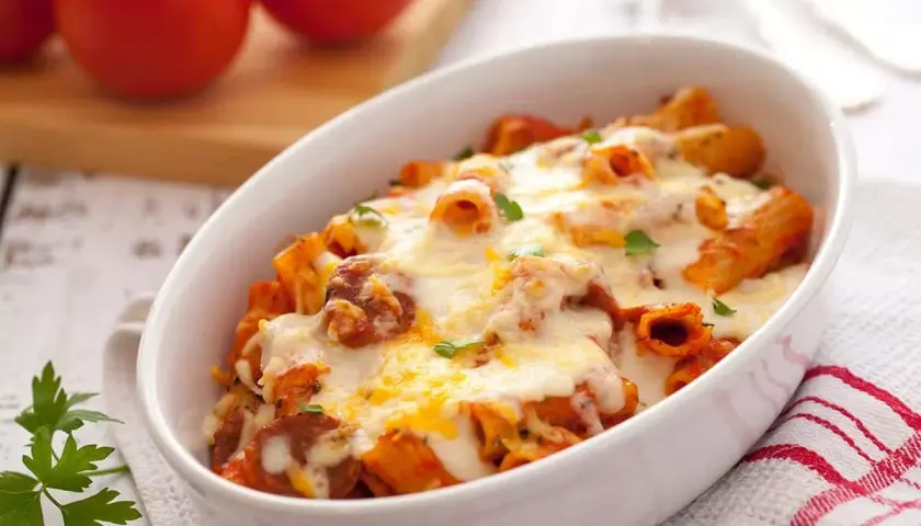 Macarrones con chorizo gratinados, cubiertos de queso derretido y perejil fresco, servidos en una fuente blanca.