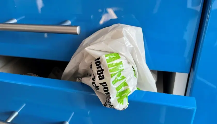 Biała reklamówka z zielonym napisem "Torba" wystaje z niebieskiej szuflady. Oto praktyczny sposób, jak przechowywać reklamówki.