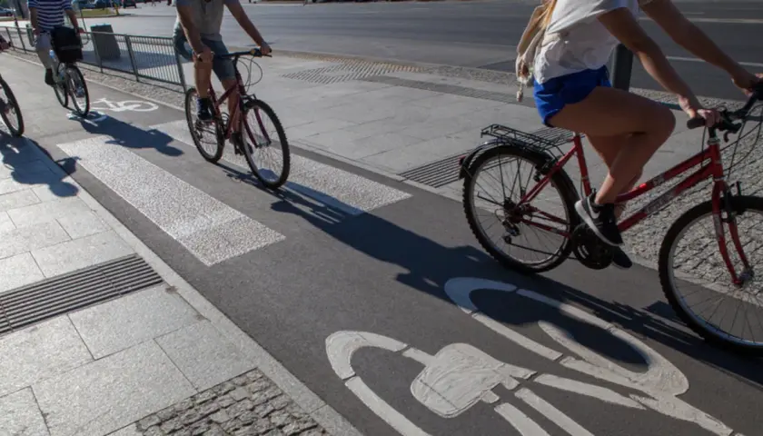 Ludzie na rowerach jadą ścieżką rowerową z oznaczeniem art 33 prd. Cienie rzucane przez rowerzystów wydłużają się na asfalcie.