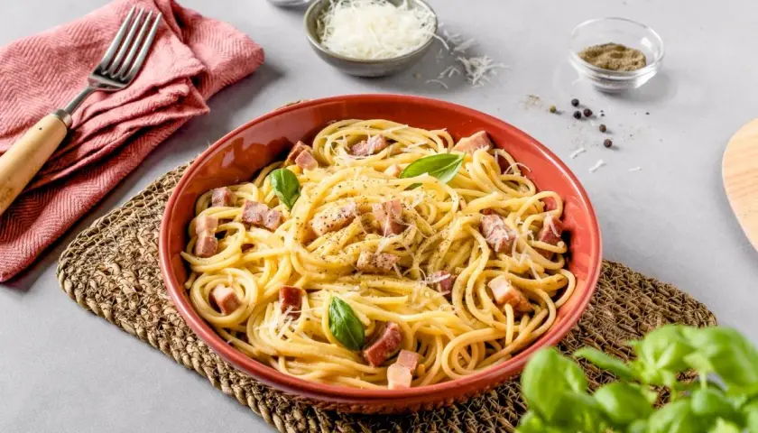 Un plato de carbonara italia, con espagueti, trozos de panceta, queso rallado y hojas de albahaca fresca.