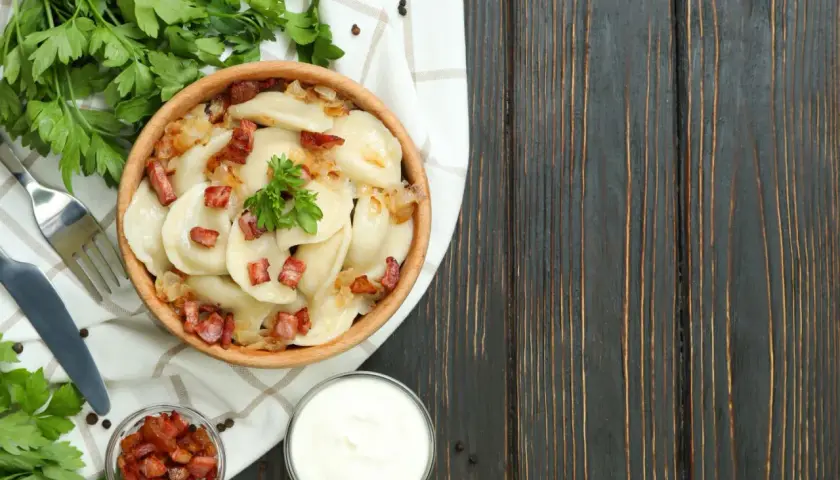 Pyszne pierogi z cebulką i skwarkami, serwowane w drewnianej misce. To klasyka kuchni łemkowskiej, podana z kwaśną śmietaną i świeżą natką pietruszki.