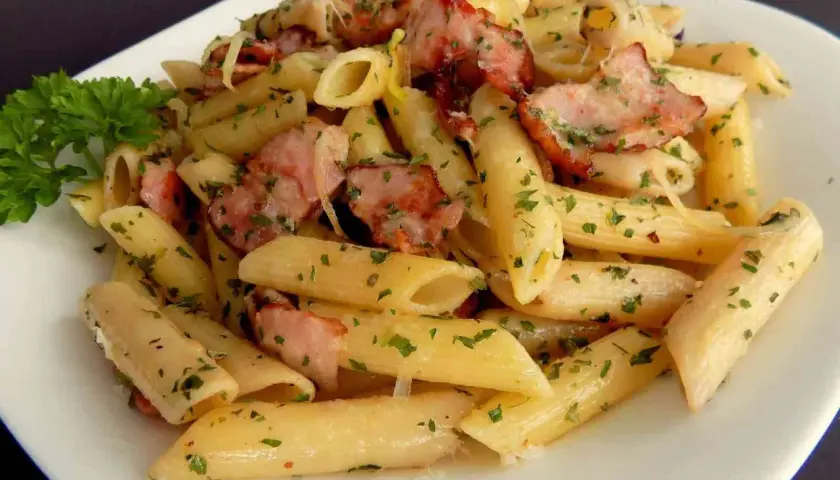 Pyszny makaron penne z kawałkami wędzonego boczku i posypany natką pietruszki. Idealny makaron na obiad.
