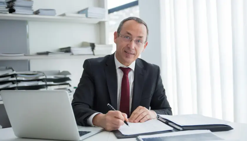 Mężczyzna w garniturze podpisuje umowę najmu u notariusza. Na biurku laptop i dokumenty.
