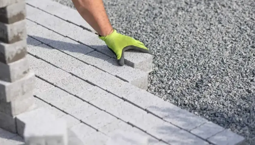 Ręka w zielonej rękawicy układa kostkę brukową na podsypce cementowo piaskowej.