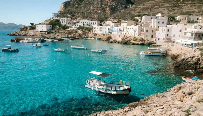 A picturesque harbor with white buildings and boats, showcasing one of the top places to see in Sicily.