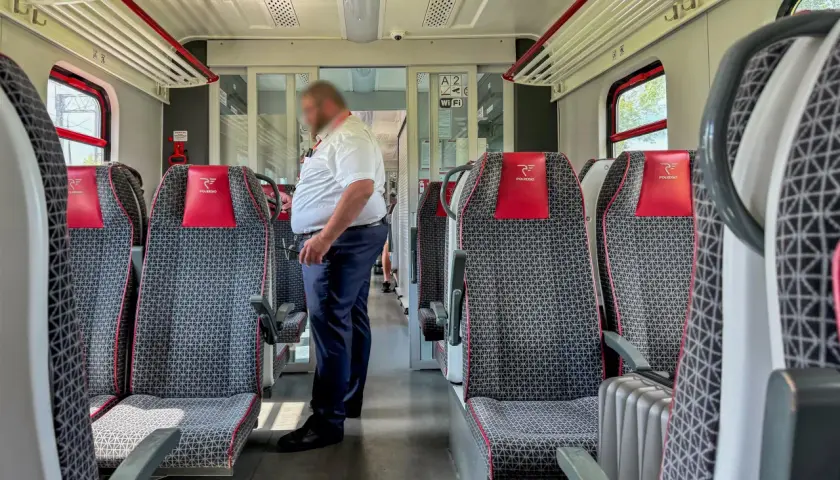 Wnętrze pociągu Polregio z siedzeniami i konduktorem. Zastanawiasz się, ile zarabia kierownik pociągu Polregio?
