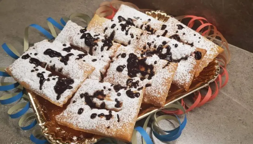 Chiacchiere morbide cosparse di zucchero a velo e gocce di cioccolato, pronte per festeggiare il Carnevale.