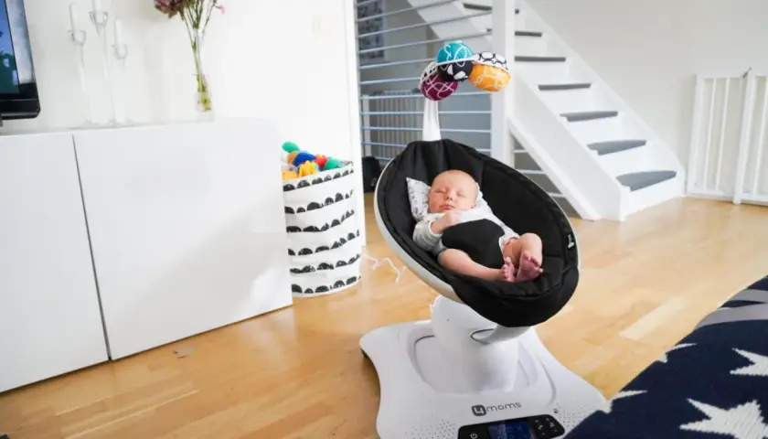 Sover gott i sin mamaroo babysitter. En bebis vilar i en svart gunga med leksaker ovanför.