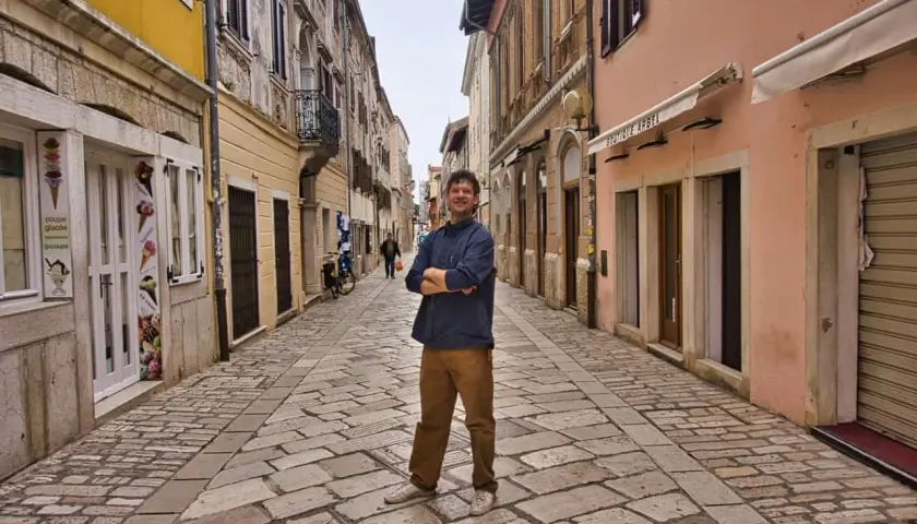 Mann steht in einer Gasse mit Kopfsteinpflaster in Poreč. Ein Eisgeschäft und Boutiquen säumen die Straße. Ein toller Ort für Poreč Geheimtipps.