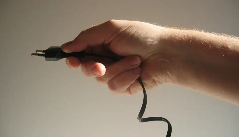 Dłoń trzymająca czarny kabel z wtyczką.
