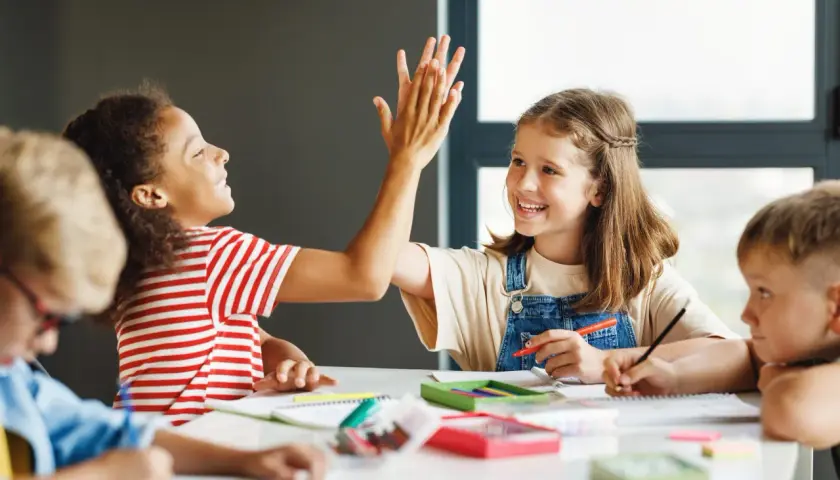 Kinder geben sich High-Five, während sie konzentriert arbeiten. Dieses Bild zeigt eigenverantwortliches Arbeiten und Freude am Lernen.