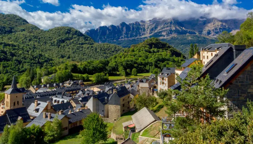 Pueblos del Pirineo Catalán, con tejados oscuros y montañas verdes de fondo bajo un cielo azul con nubes.