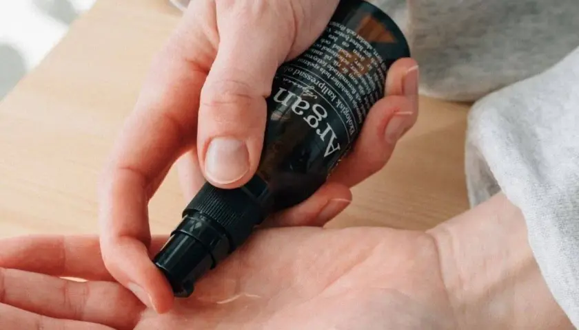 En hand pumpar ut arganolja i en annan handflata. Oljan är ekologisk och kallpressad.