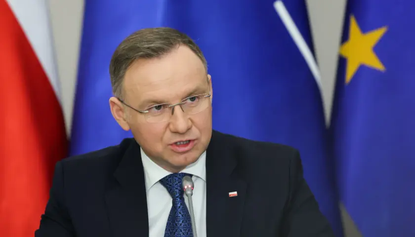 Andrzej Duda w garniturze, za nim flagi Polski i UE. Prawdziwe powody dla których Andrzej Duda zapowiedział serię wet do ustaw budżetowych.