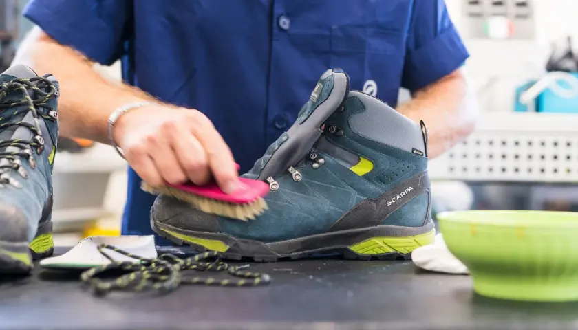 A person is cleaning a hiking boot with a brush, demonstrating how to maintain shoes.