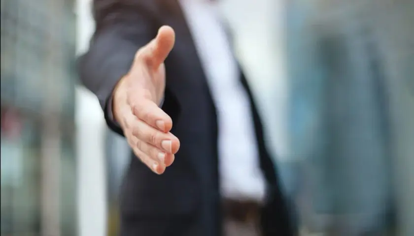 Biznesmen wyciąga rękę do uścisku, symbolizując partnerstwo i współpracę. Dowiedz się, jak założyć spółkę cywilną.