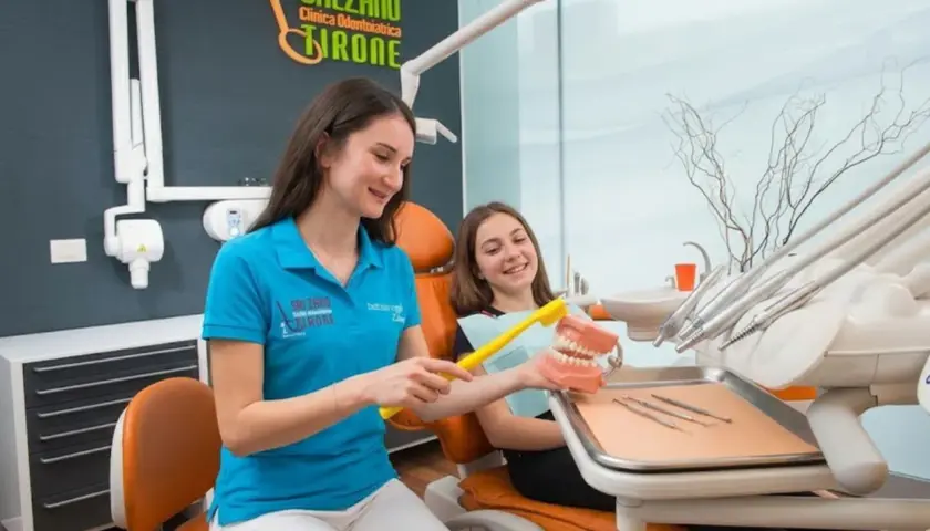Dentista mostra a una bambina come lavarsi i denti su un modello. Scopri il detartrasi costo per un sorriso smagliante.