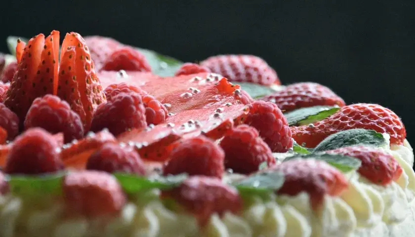 Pyszny tort dobosza, udekorowany malinami, truskawkami i listkami mięty, posypany srebrnymi kuleczkami.