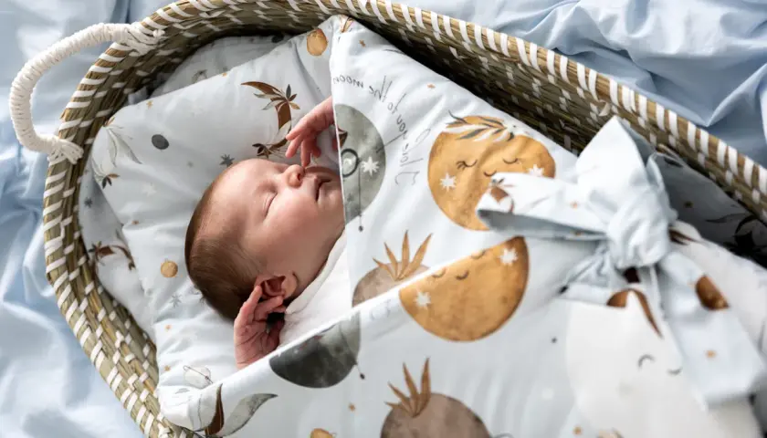 Śpiące dziecko otulone rożkiem niemowlęcym z motywem księżyców i gwiazdek. Idealny wybór dla maluszka.