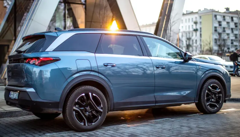 Niebieski Peugeot 5008 na tle nowoczesnej architektury. Wiele osób szuka peugeot 5008 opinie przed zakupem.