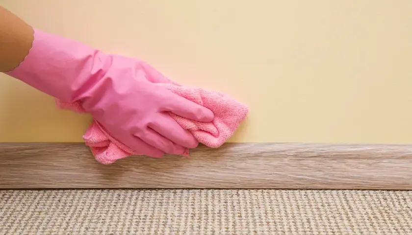 Mano con guanto rosa pulisce la pittura lavabile con un panno rosa.