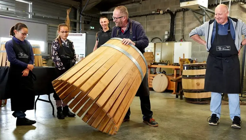 Visite tonnellerie Bourgogne : un maître tonnelier montre un fût en cours de fabrication à des apprentis.
