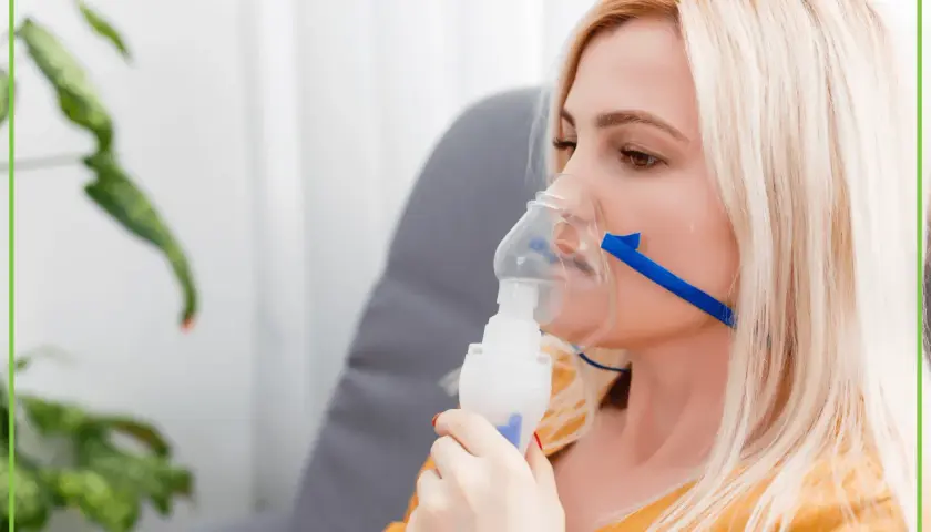 Kobieta z blond włosami używa nebulizatora, co może być częścią terapii w chorobie takiej jak mukowiscydoza.
