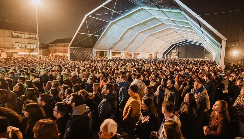 Multitudinaria asistencia al concierto astillero hoy bajo una gran carpa. La gente disfruta de la música y el ambiente nocturno.