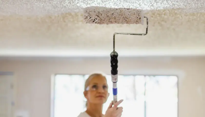 Donna imbianca il soffitto con un rullo, un modo semplice per rinnovare casa.