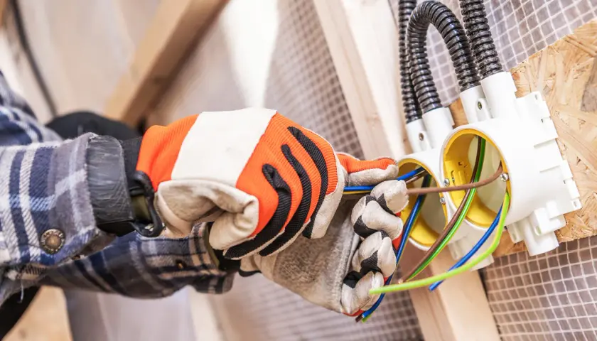 Ręce w rękawicach montują puszki elektryczne. To etap prac, który wpływa na to, ile kosztuje założenie instalacji elektrycznej w domu.