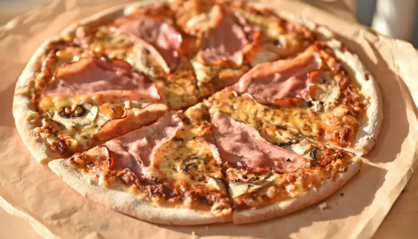 Pyszna pizza z szynką i pieczarkami na pizze, zrumieniona i apetyczna, leży na papierze.