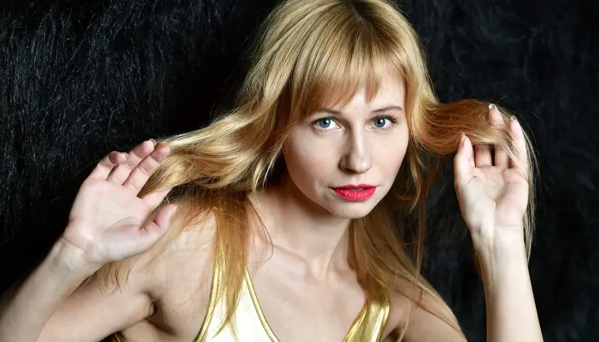 Kobieta z blond grzywką i niebieskimi oczami, zastanawiająca się, ile rośnie grzywka w tydzień.