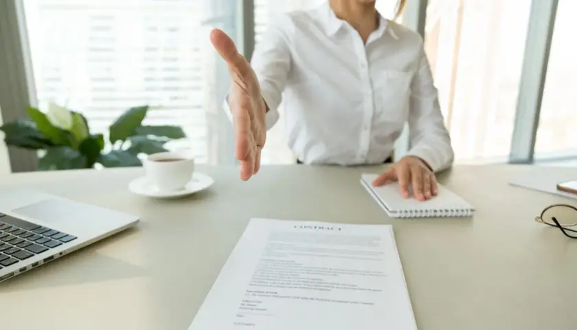 Bizneswoman wyciąga rękę do uścisku nad dokumentem "CONTRACT". Może to być umowa, wykreślenie hipoteki lub inny ważny wpis.